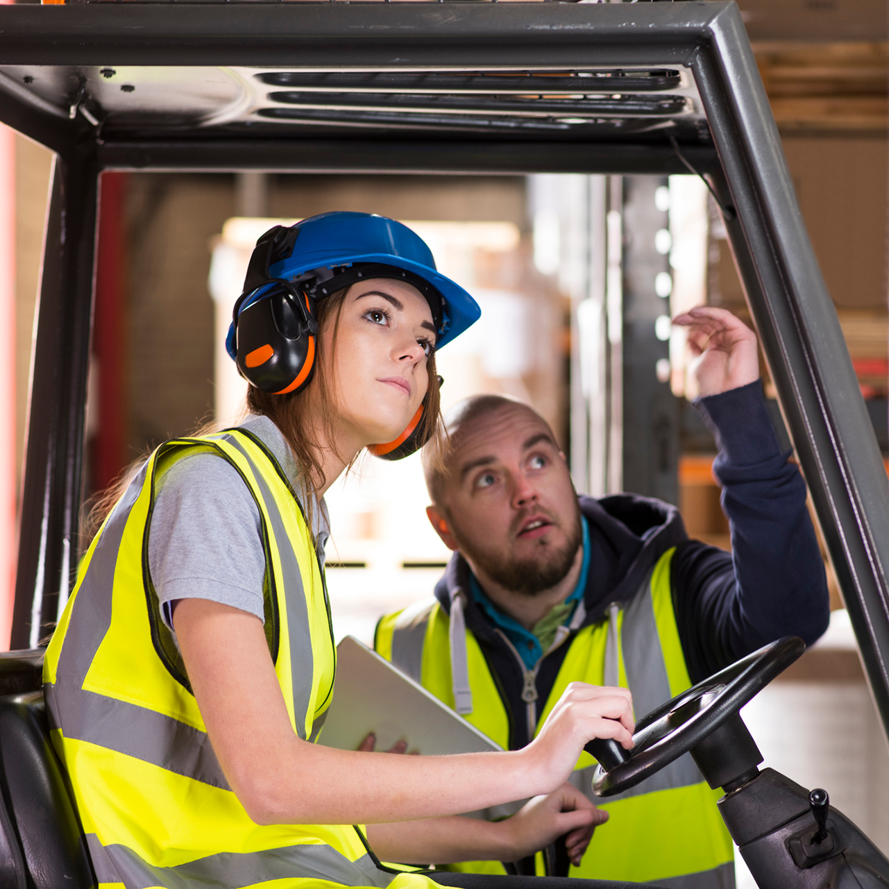Female construction worker in safety vest and hard hat at a worksite with coworker giving instructions